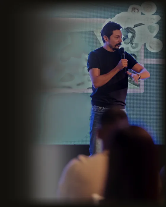 Adriano Figueiredo falando ao microfone num palco, diante de plateia
